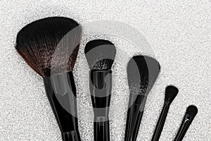 Black and brown makeup brushes on shiny silver background surface