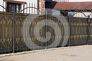 Black brown metal fence with forged pattern on the street