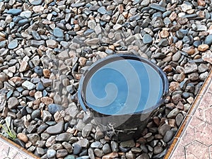 Black bucked filled with rainwater on the small stones of the river in the yard