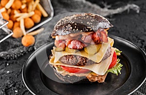 Black burger with beaf steak, lettuce, tomatoes, slice of cheese, ham, pastrami and sauce on slate black background, top view