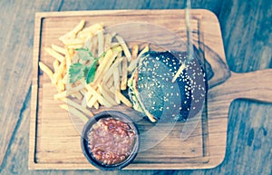 Black burger with french fries in a wooden plate.