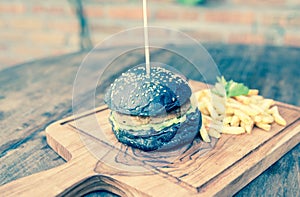 Black burger with french fries in a wooden plate.