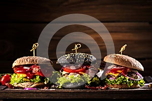 Black burger with meat patty, cheese, tomatoes, mayonnaise. Dark wooden rustic table. Modern fast food lunch