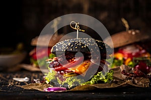 Black burger with meat patty, cheese, tomatoes, mayonnaise. Dark wooden rustic table. Modern fast food lunch