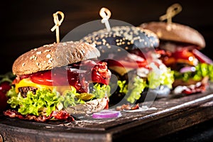 Black burger with meat patty, cheese, tomatoes, mayonnaise. Dark wooden rustic table. Modern fast food lunch