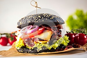 Black burger with meat patty, cheese, tomatoes, mayonnaise. Dark wooden rustic table. Modern fast food lunch