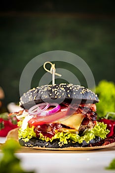 Black burger with meat patty, cheese, tomatoes, mayonnaise. Dark wooden rustic table. Modern fast food lunch