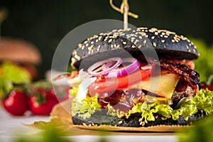Black burger with meat patty, cheese, tomatoes, mayonnaise. Dark wooden rustic table. Modern fast food lunch