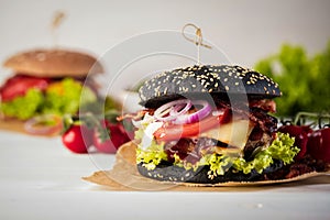 Black burger with meat patty, cheese, tomatoes, mayonnaise. Dark wooden rustic table. Modern fast food lunch