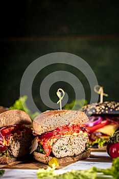 Black burger with meat patty, cheese, tomatoes, mayonnaise. Dark wooden rustic table. Modern fast food lunch