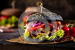 Black burger with meat patty, cheese, tomatoes, mayonnaise. Dark wooden rustic table. Modern fast food lunch