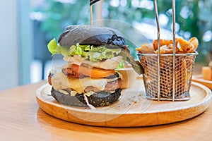 Black burger with meat patty, cheese, tomatoes, mayonnaise, french fries in a paper cup and glass of cold cola soda with ice.