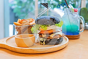 Black burger with meat patty, cheese, tomatoes, mayonnaise, french fries in a paper cup and glass of cold cola soda with ice.