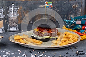 Black burger with meat patty, cheese, tomatoes, mayonnaise, french fries in a paper. Dark stone background. Modern fast