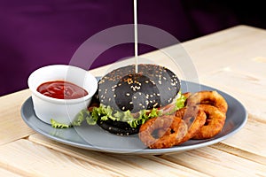Black burger with meat tomato sause and potato rings on the wooden table