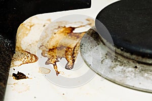 Black burner and burnt fat on the white surface of the kitchen stove