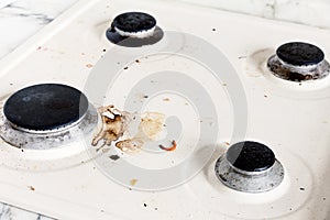 Black burner and burnt fat on the white surface of the kitchen stove