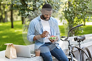 Black businessman having salad for lunch and working on laptop outdoor