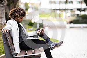 Black businessman in suit using laptop while sitting on bench near modern office building, side view, free space