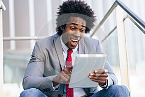 Black Businessman using a digital tablet sitting near an office building. photo