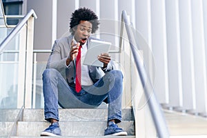 Black Businessman using a digital tablet sitting near an office building. photo