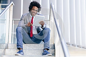 Black Businessman using a digital tablet sitting near an office building. photo