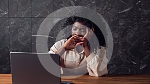 Black businesswoman with curly hair types on laptop lazily