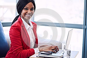 Black businesswoman looking into camera with her hands on laptop