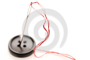 Black button, needle with red thread close up macro shot isolated