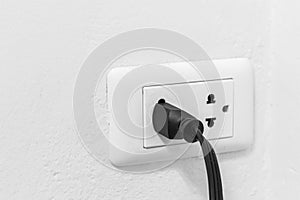 Black cable plugged in a white electric outlet on whith wall