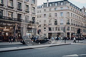 Black cabs waiting on a red traffic light on Regent Street, London, UK, shops on the background