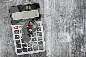 A black calculator with car keys on weathered wood desk