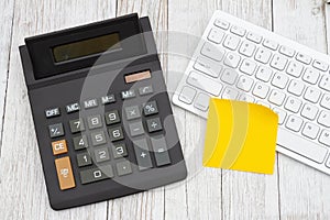 A black calculator with computer keyboard on wood desk