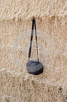 A black camera bag hangs against a wall of dry straw. A small wa