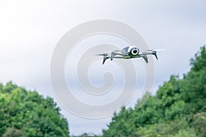 Black camera drone in flying with visible propellers movement and in blue sky background