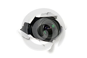 Black camera with a telephoto lens that looks out through a hole in white paper. Concept of paparazzi, espionage, yellow