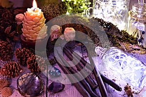 Black candles, cones, nature elements and shining bottle on table