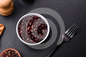 Black, canned beans in a white saucer against a dark concrete background