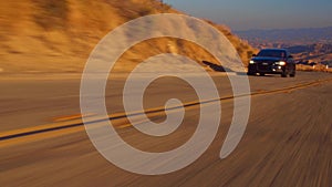 Black car Audi A6 with driving on mountains road during sunset and mountains in background low light shot. Highway in the mountain