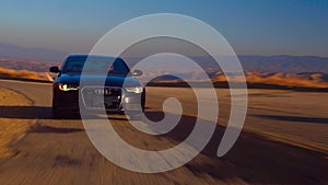 Black Car Audi A6 with driving on mountains road during sunset and mountains in background low light shot. Highway in the mountain