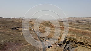 Black car driving on asphalt road through the desert sands, the camera flies over the land