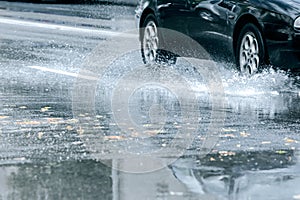 Black car driving through rain puddle with splashing water from