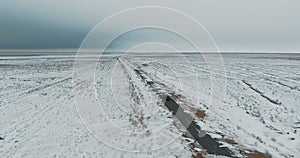 Black car driving on winter country road in snowy forest, aerial view from drone