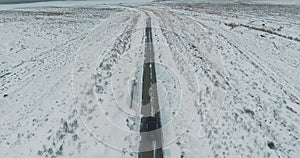 Black car driving on winter country road in snowy forest, aerial view from drone