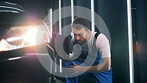 Black car is getting inspected by a male technician with a computer