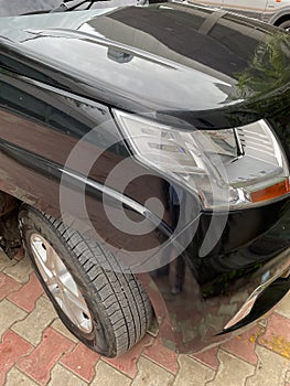 A black car with its tyre, head light and front side facade