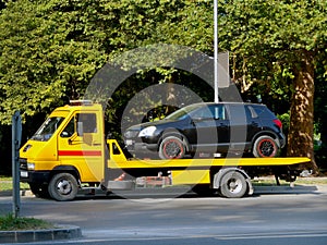 Black car is loaded on a yellow car tow truck on a city street