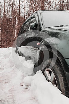 black car parked in snowdrift. Auto covered in snow. Wheel stuck in the deep snow