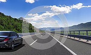 Black car rushes along the road against the backdrop of a beautiful countryside landscape.