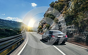 Black car rushing along a high-speed highway in the sun.